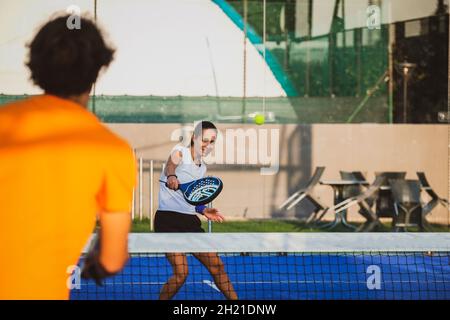 Der junge Lehrer überwacht den Padel-Unterricht für seine Schülerin - Coach lehrt Mädchen, wie man Padel auf dem Tennisplatz im Freien spielt Stockfoto