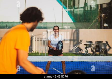 Der junge Lehrer überwacht den Padel-Unterricht für seine Schülerin - Coach lehrt Mädchen, wie man Padel auf dem Tennisplatz im Freien spielt Stockfoto