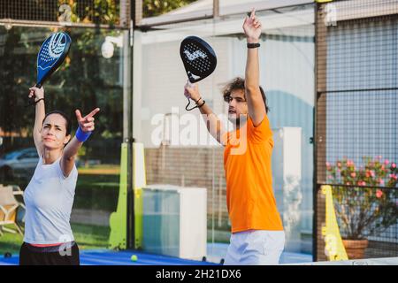 Der junge Lehrer überwacht den Padel-Unterricht für seine Schülerin - Coach lehrt Mädchen, wie man Padel auf dem Tennisplatz im Freien spielt Stockfoto