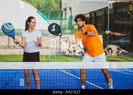 Der junge Lehrer überwacht den Padel-Unterricht für seine Schülerin - Coach lehrt Mädchen, wie man Padel auf dem Tennisplatz im Freien spielt Stockfoto