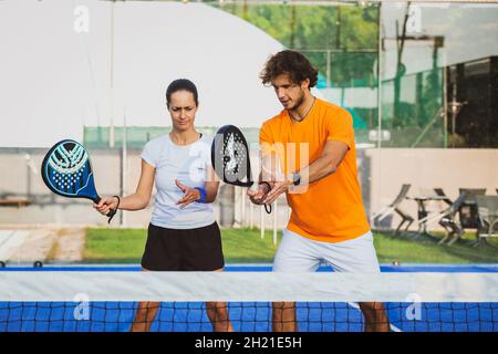 Der junge Lehrer überwacht den Padel-Unterricht für seine Schülerin - Coach lehrt Mädchen, wie man Padel auf dem Tennisplatz im Freien spielt Stockfoto