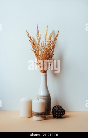 Trockene Pampagras in Vase, Tannenzapfen und Kerzen auf einem Tisch gegen weiße Wand. Stillleben. Einrichtung im Boho-Stil. Stockfoto