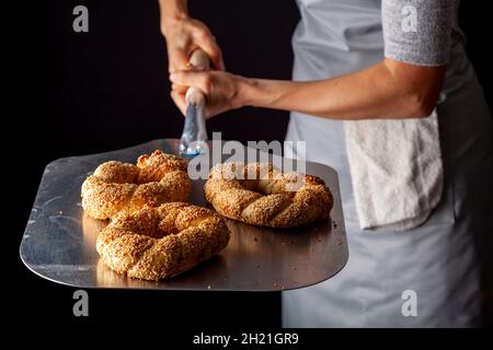 Köstlicher türkischer Bagel mit Sesamsamen, bekannt als Susamli simit. Heiß aus dem Steinofen auf einem großen Pizzaschälchen serviert. Ein Bäcker hält es tigh Stockfoto