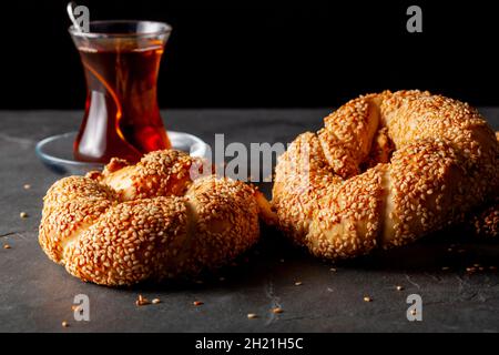 Köstlicher türkischer Bagel mit Sesamsamen, bekannt als Susamli simit. Nahaufnahme Einzelbild mit zwei frisch gebackenen Brötchen, serviert mit schwarzem Tee im Glas Stockfoto