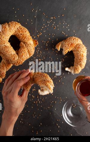 Köstlicher türkischer Bagel mit Sesamsamen, bekannt als Susamli simit. Eine Frau isst ein Stück Bagel und hält eine Tasse schwarzen Tee in der Hand. Flach Stockfoto