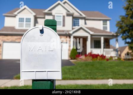 Nahaufnahme eines isolierten Bildes eines weiß lackierten Briefkastens aus Metall vor einem einsamen Vorstadthaus mit grünem Rasen. Konzept-Image für Mail-Dalivery Stockfoto