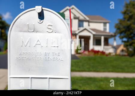 Nahaufnahme eines isolierten Bildes eines weiß lackierten Briefkastens aus Metall vor einem einsamen Vorstadthaus mit grünem Rasen. Konzept-Image für Mail-Dalivery Stockfoto
