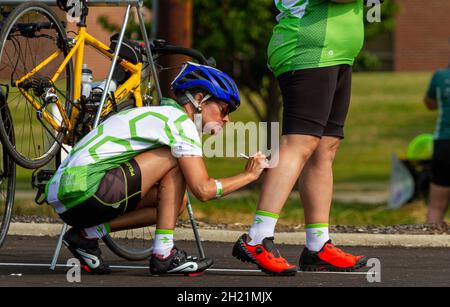 Columbus, OH USA 08-07-2021: Eine junge kaukasische Frau, die Fahrradanzüge und Helm trägt, schreibt etwas auf das Bein ihrer Teamkollegin, um sie zu unterstützen Stockfoto