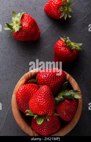Eine Holzschale mit Erdbeeren auf einer dunklen Tischplatte. Schwaches, launiges Bild mit gesunden Snacks und frischen Fruchtkonzepten. Flach liegend, Draufsicht Stockfoto