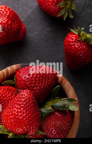 Nahaufnahme eines isolierten Bildes einer hölzernen Holzschüssel, gefüllt mit frischen, rohen Erdbeeren auf dunklem Steingrund. Voll von Nährstoffen, rohe Bio-Lebensmittel für ihn Stockfoto