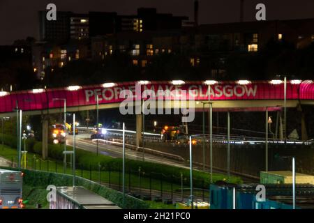 Glasgow, Schottland, Großbritannien. Oktober 2021. IM BILD: Menschen machen Glasgow Walkway über den Clydeside Expressway. Nachtansicht des COP26-Geländes und des Veranstaltungsortes mit temporären Strukturen, die zur Hälfte auf dem Gelände des Scottish Event Campus (SEC) errichtet wurden, das früher als Scottish Exhibition and Conference Center (SECC) bekannt war, mit dem vorderen Parkplatz außerhalb des neu benannten OVO Hydro (ehemals SSE Hydro) Mit neuen Transfers über den Steg, die sagen, „die Menschen machen Glasgow“ und Nachtarbeiter machen weiterhin Vorbereitungen. Quelle: Colin Fisher/Alamy Live News Stockfoto