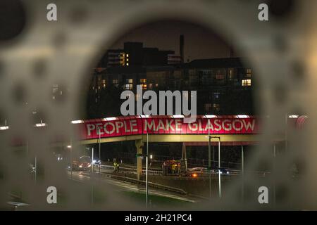 Glasgow, Schottland, Großbritannien. Oktober 2021. IM BILD: Menschen machen Glasgow Walkway über den Clydeside Expressway. Nachtansicht des COP26-Geländes und des Veranstaltungsortes mit temporären Strukturen, die zur Hälfte auf dem Gelände des Scottish Event Campus (SEC) errichtet wurden, das früher als Scottish Exhibition and Conference Center (SECC) bekannt war, mit dem vorderen Parkplatz außerhalb des neu benannten OVO Hydro (ehemals SSE Hydro) Mit neuen Transfers über den Steg, die sagen, „die Menschen machen Glasgow“ und Nachtarbeiter machen weiterhin Vorbereitungen. Quelle: Colin Fisher/Alamy Live News Stockfoto