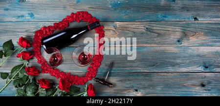 Valentinstag Urlaub Hintergrund mit roten Rosen, Weinflasche, Trinkgläser und kleine Herzformen bilden großen Herzumriss auf verblichenen blauen Holz Stockfoto