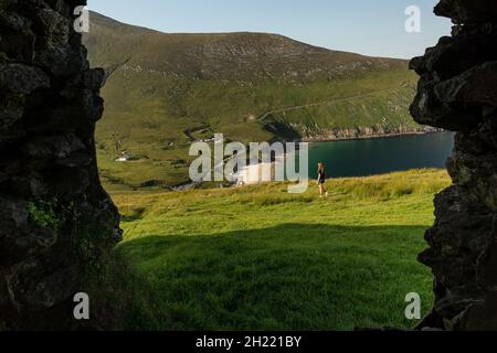 Durch ein Fenster eines alten Gebäudes. Eine kaukasische Reisende Frau in Keem Bay Achill Island, Irland Stockfoto