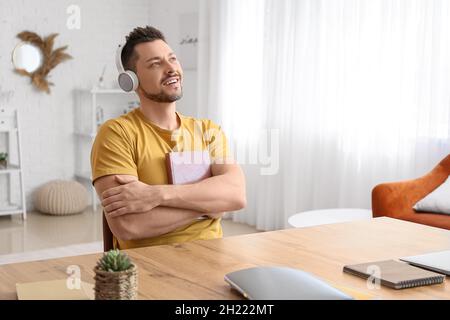 Mann mit Kopfhörern hört Hörbuch am Tisch Stockfoto