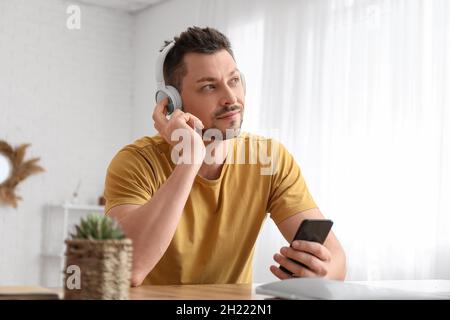 Mann mit Telefon und Kopfhörer am Tisch Stockfoto