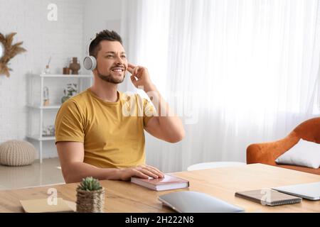 Mann mit Kopfhörern hört Hörbuch am Tisch Stockfoto