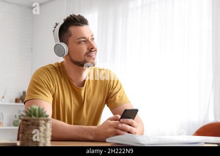Mann mit Telefon und Kopfhörer am Tisch Stockfoto
