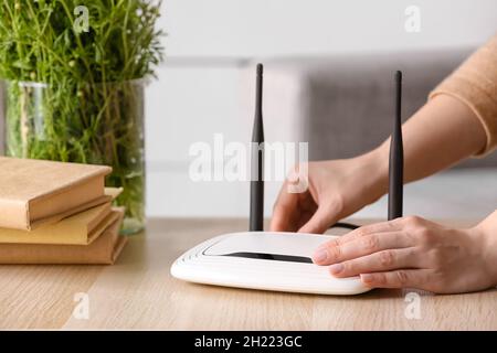 Frau, die Ethernet-Kabel in den wi-Fi-Router auf dem Tisch im Zimmer eingeführt hat Stockfoto