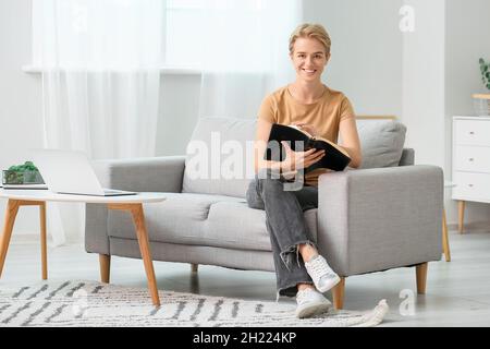 Junge Frau, die zu Hause auf dem Sofa die Heilige Bibel liest Stockfoto