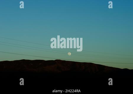 Der Mond steigt über den Bergen in Südkalifornien, wobei die Stromleitungen im Vordergrund verlaufen. Stockfoto