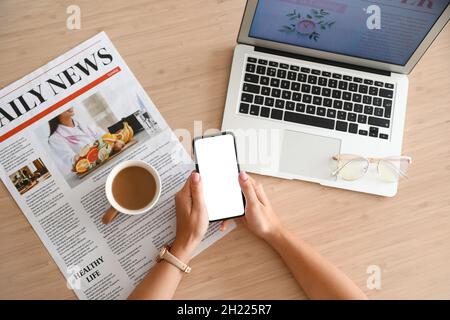 Weibliche Hände mit Handy, Zeitung, Laptop und Tasse Kaffee auf Holztisch Stockfoto