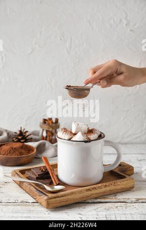 Frau streut Kakaopulver in den Becher mit leckerer heißer Schokolade auf dem Tisch Stockfoto