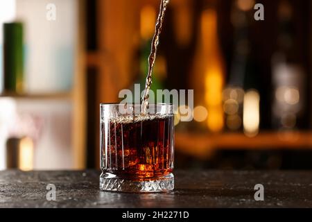 Cuba Libre Cocktail in Glas auf dunklem Tisch gießen Stockfoto