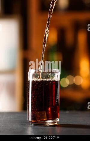 Cola in Glas mit Cuba Libre Cocktail auf dunklem Tisch gießen Stockfoto