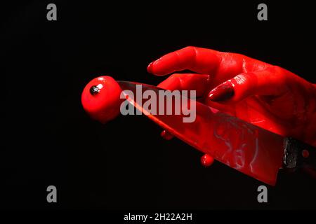 Hand mit blutbeflecktem Messer und Augenball auf schwarzem Hintergrund Stockfoto