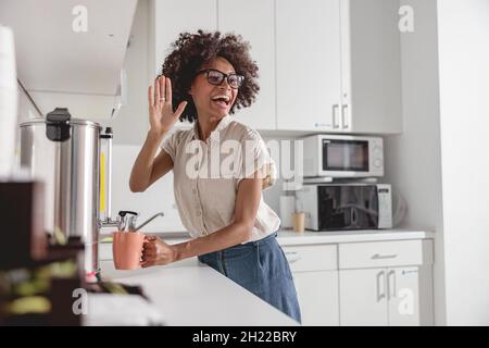 Lächelnde junge Frau, die in der Küche Tee in eine Tasse gießt Stockfoto