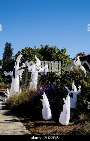 Große Versammlung von mindestens acht luftdurchgeblasenen aufblasbaren Geistern, die auf dem Bürgersteig in einer Wohnstraße im sonnigen Kalifornien zu Halloween-Feiern gegenüberstehen Stockfoto