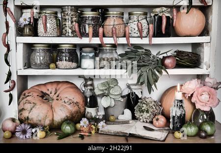 Grunge Stillleben mit brennender Kerze, Bohne in alten Flaschen und Gläsern, Kürbis, hängender Paprika, grüne Tomaten. Klassisches Küchenkonzept. Provence, Stockfoto