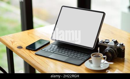 Modernes Gerätekonzept, moderner digitaler Tablet-Computer mit leerem Bildschirm, Modell mit Smartphone, Kamera und Kaffeetasse auf dem Tisch. Stockfoto