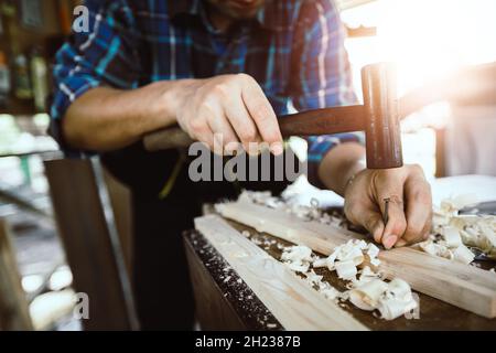 Nahaufnahme eines Zimmermanns, der im Laden arbeitet, und Schlag einen Nagel durch Hummer auf Holz Stockfoto