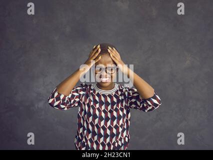 Junge schwarze Frau, die ihren Kopf hält, fühlt sich gestresst und von Emotionen überwältigt Stockfoto