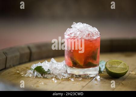 Nahaufnahme eines Glases roten Alkoholcocktails auf einem Holzfass Stockfoto