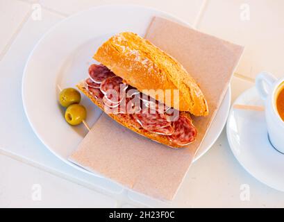 Spanisches Frühstück: Geräuchertes Würstchen-Fuet-Sandwich und Oliven in der Nähe Stockfoto