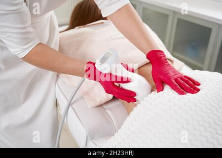 Junge Frau bekommt fettreduktive Haut Lifting Körperbehandlung durch einen Kosmetologen. Attraktive weibliche Patientin, die sich gerne an schlankeren Körperkonturierung erfreut Stockfoto