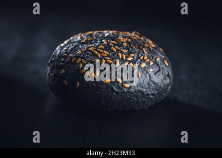 Schwarzes Brötchen. Dunkles Gebäck mit Sesam auf schwarzem Tisch. Stockfoto