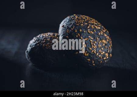 Schwarzes Brötchen. Dunkles Gebäck mit Sesam auf schwarzem Tisch. Stockfoto