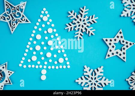 Weiße runde Pillen, die in Form eines Weihnachtsbaums mit hölzernen Schneeflocken auf hellblauem Hintergrund ausgelegt sind. Flach liegend Stockfoto