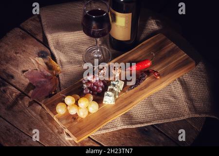 Rotwein-Flasche, Traube, Käse, Weinglas und Chili-Pfeffer auf Holzbrett Stockfoto