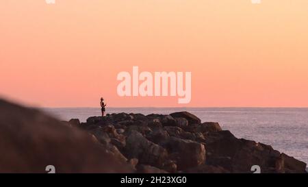 Frau, die auf Felsen steht und den Sonnenaufgang beobachtet Stockfoto