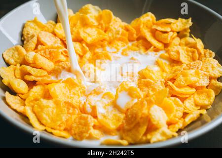 Gießen von Milch in Schüssel mit Cornflakes auf dem rustikalen Hintergrund. Selektiver Fokus. Geringe Schärfentiefe. Stockfoto