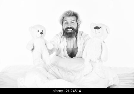 Gute Stimmung. Verspielt und romantisch. Mann umarmt Spielzeug entspannen im Bett. Imaginäre Freunde. Bemühen Sie sich, gute Schlafgewohnheiten zu üben. Niedliche Teddybär Spielzeug. Positiv Stockfoto