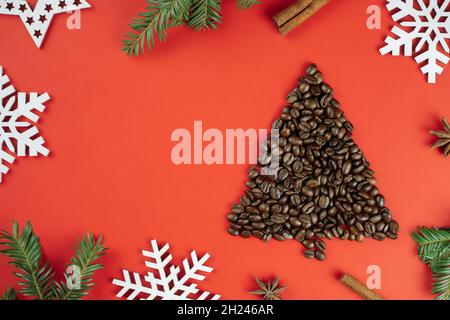 Braune Kaffeebohnen in Form eines Weihnachtsbaums mit Fichtenzweigen und hölzernen Schneeflocken auf rotem Hintergrund. Flach liegend. Speicherplatz kopieren Stockfoto