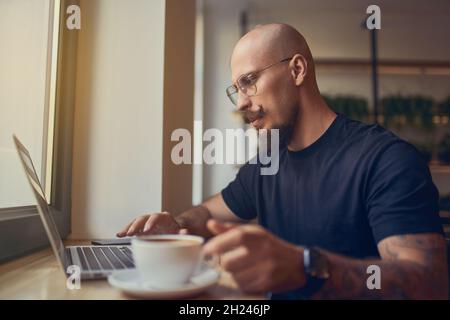 Fokussierter Geschäftsmann arbeitet am pc, analysiert die Ergebnisse der Verkaufszahlen, lernt Grafiken, während er im Café sitzt Stockfoto