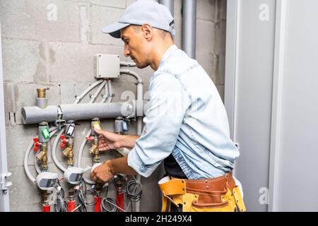 Männlicher Klempner prüft Rohre für zentrale heiß- und Kaltwasserversorgung der Wohnung Stockfoto