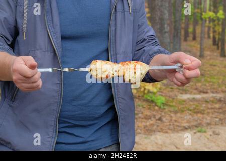 Gegrilltes Fleisch in den Händen eines Mannes in der Natur. Shish Kebab Braten auf dem Grill im Freien. Stockfoto